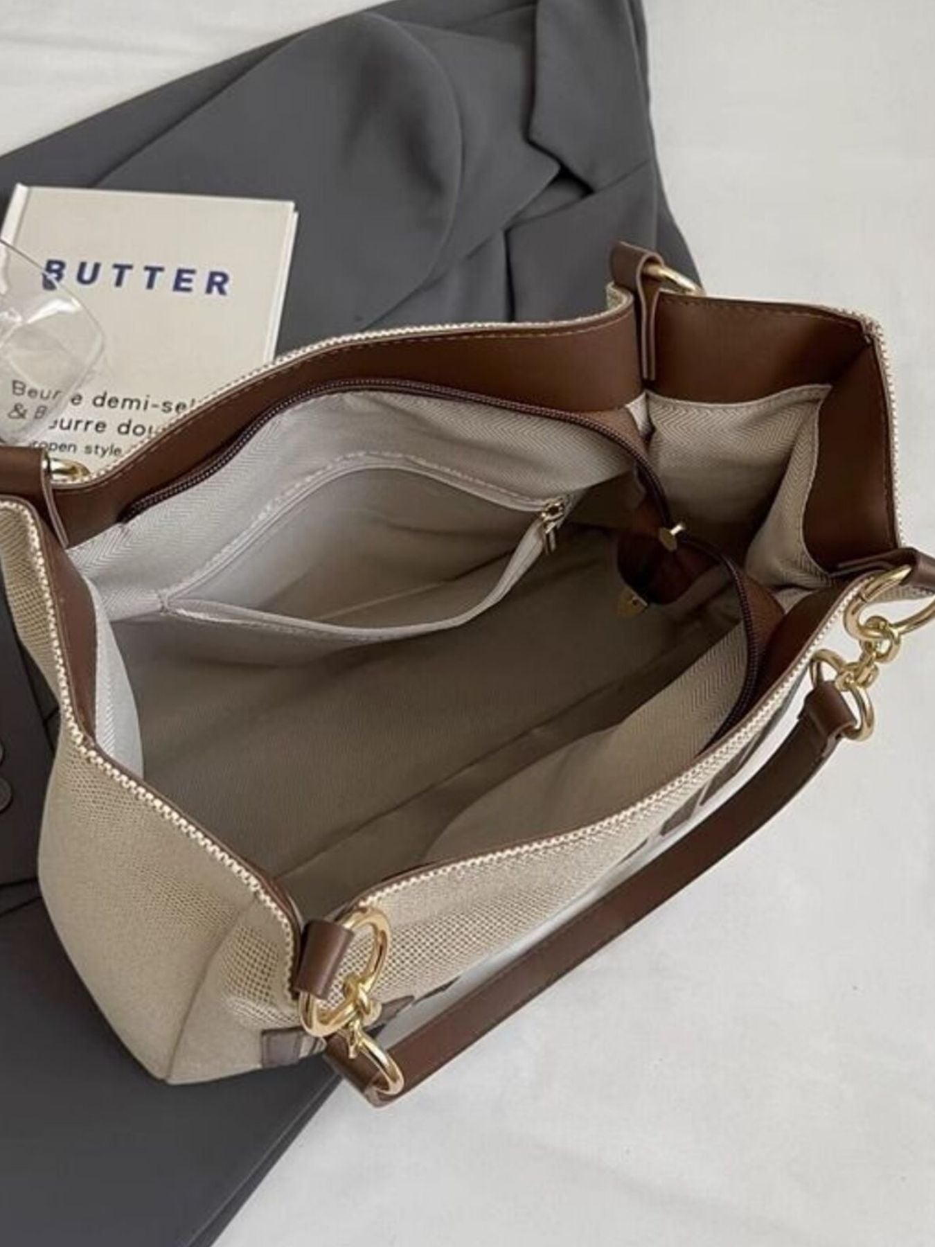 Textured canvas shoulder bag with brown trim and gold chain accents, open interior view.