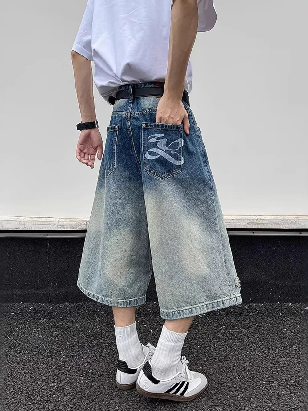 Men's distressed wide-leg denim shorts with gradient wash and graphic back pocket detail.