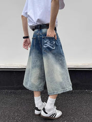 Men's distressed wide-leg denim shorts with gradient wash and graphic back pocket detail.
