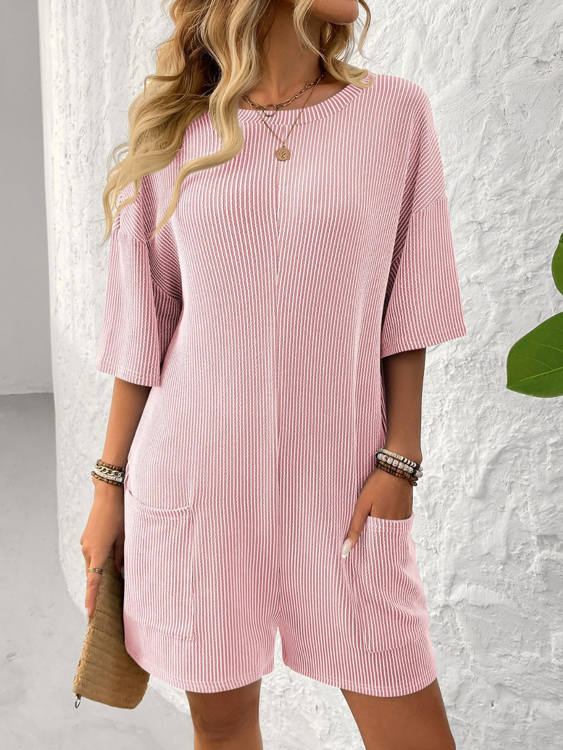 Blush pink ribbed knit romper with short sleeves, crew neck, and two front pockets.