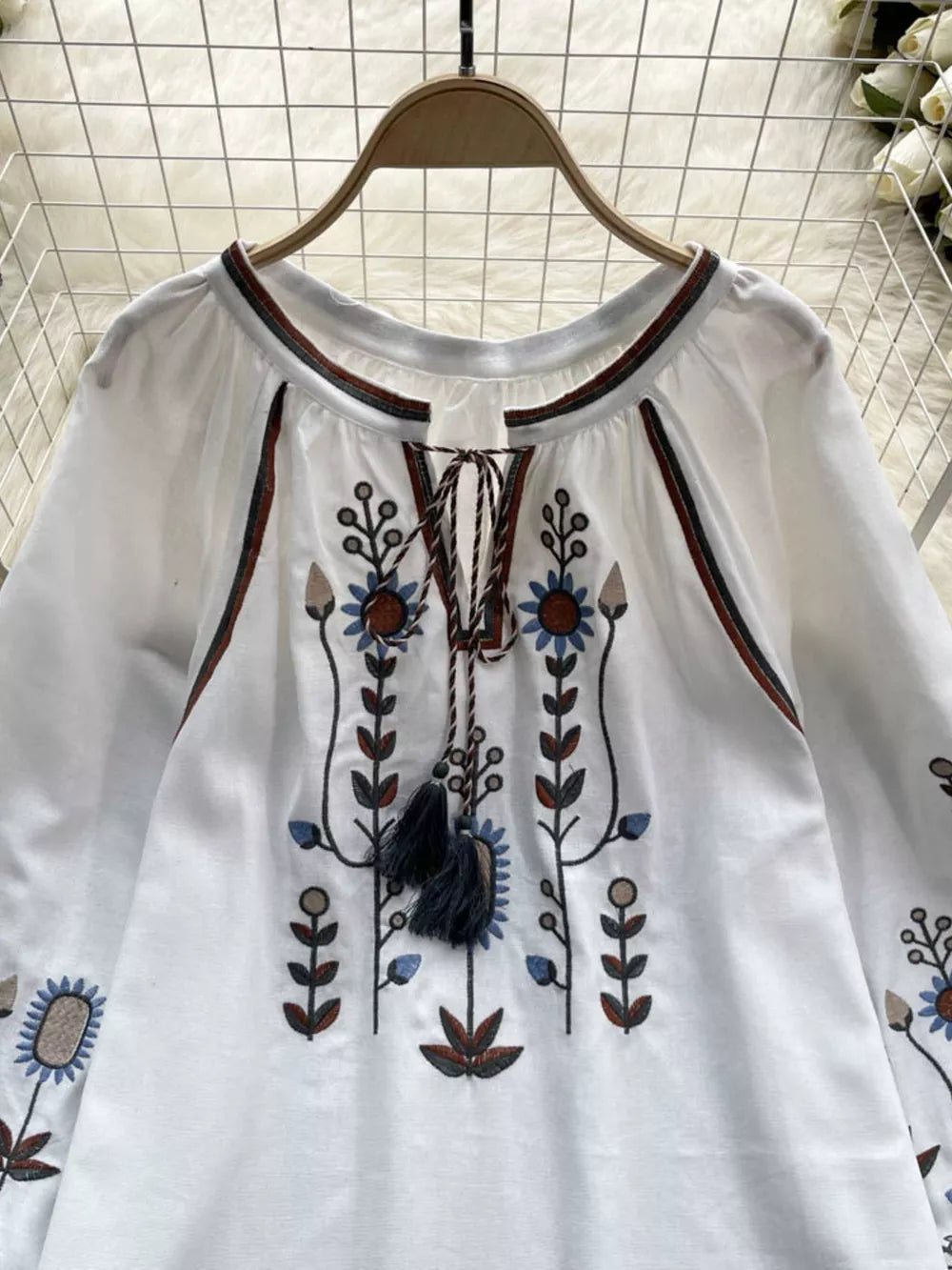 White blouse with tie neck, billowy sleeves, and colorful floral embroidery.
