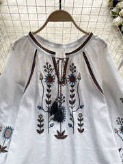 White blouse with tie neck, billowy sleeves, and colorful floral embroidery.