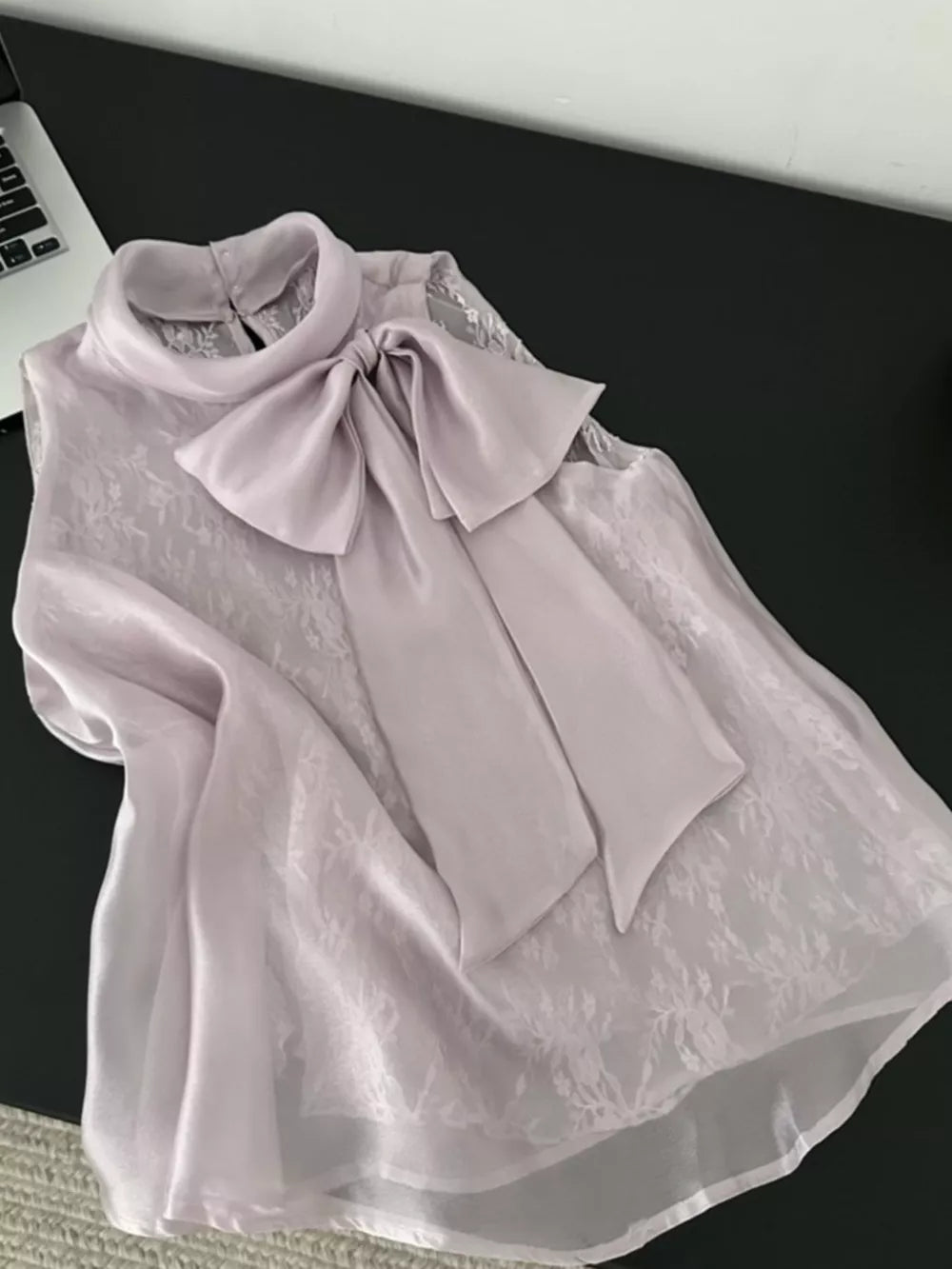 Sleeveless purple shirt with lace overlay and large satin bow detail.