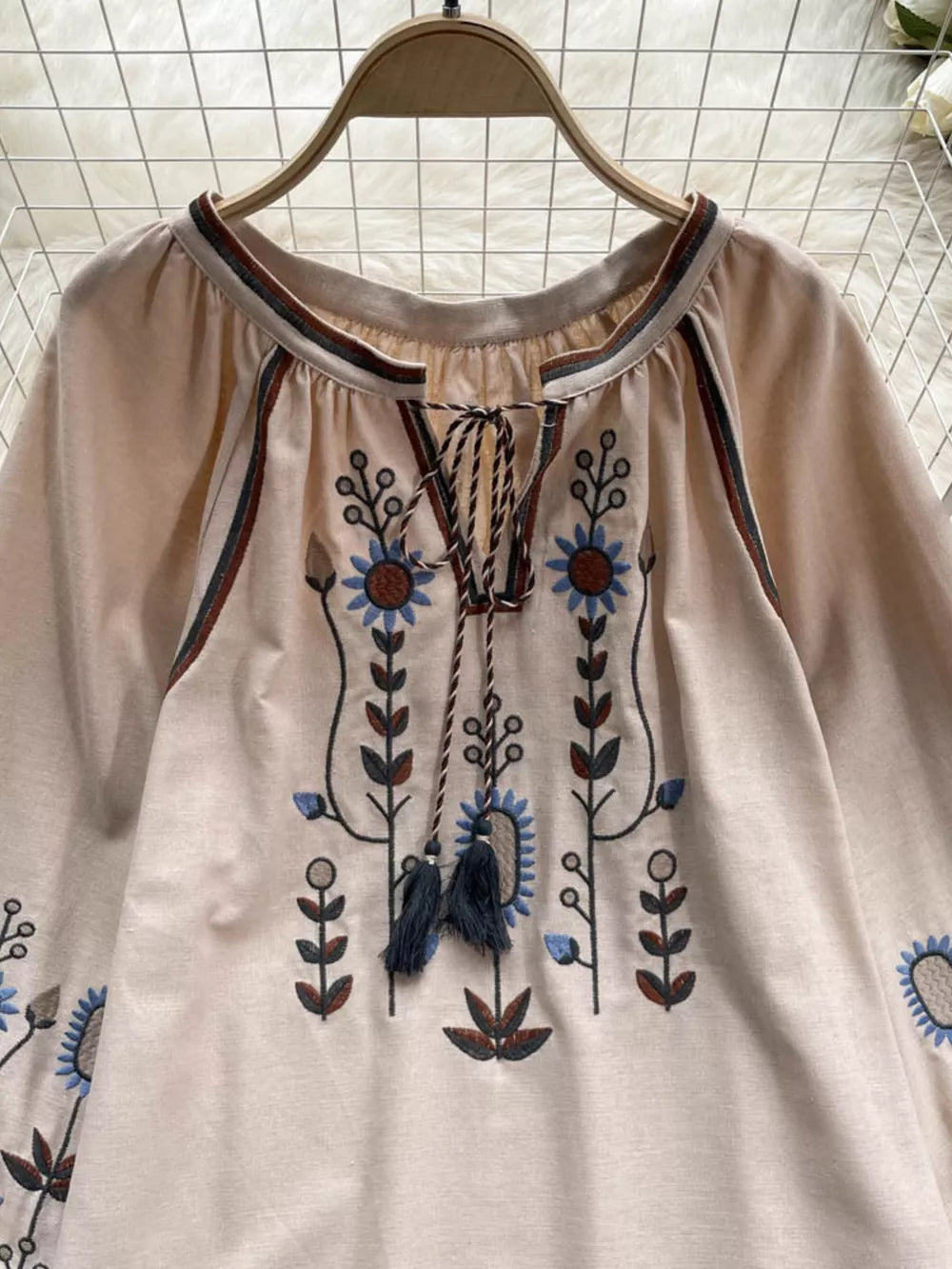 Apricot tie neck blouse with floral embroidery and tassels.