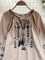Apricot tie neck blouse with floral embroidery and tassels.