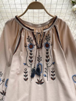 Apricot tie neck blouse with floral embroidery and tassels.