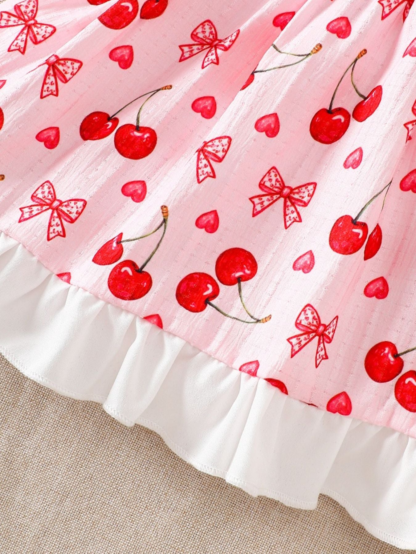 Baby dress with cherry and bow print on pink cotton, featuring a white ruffle hem.