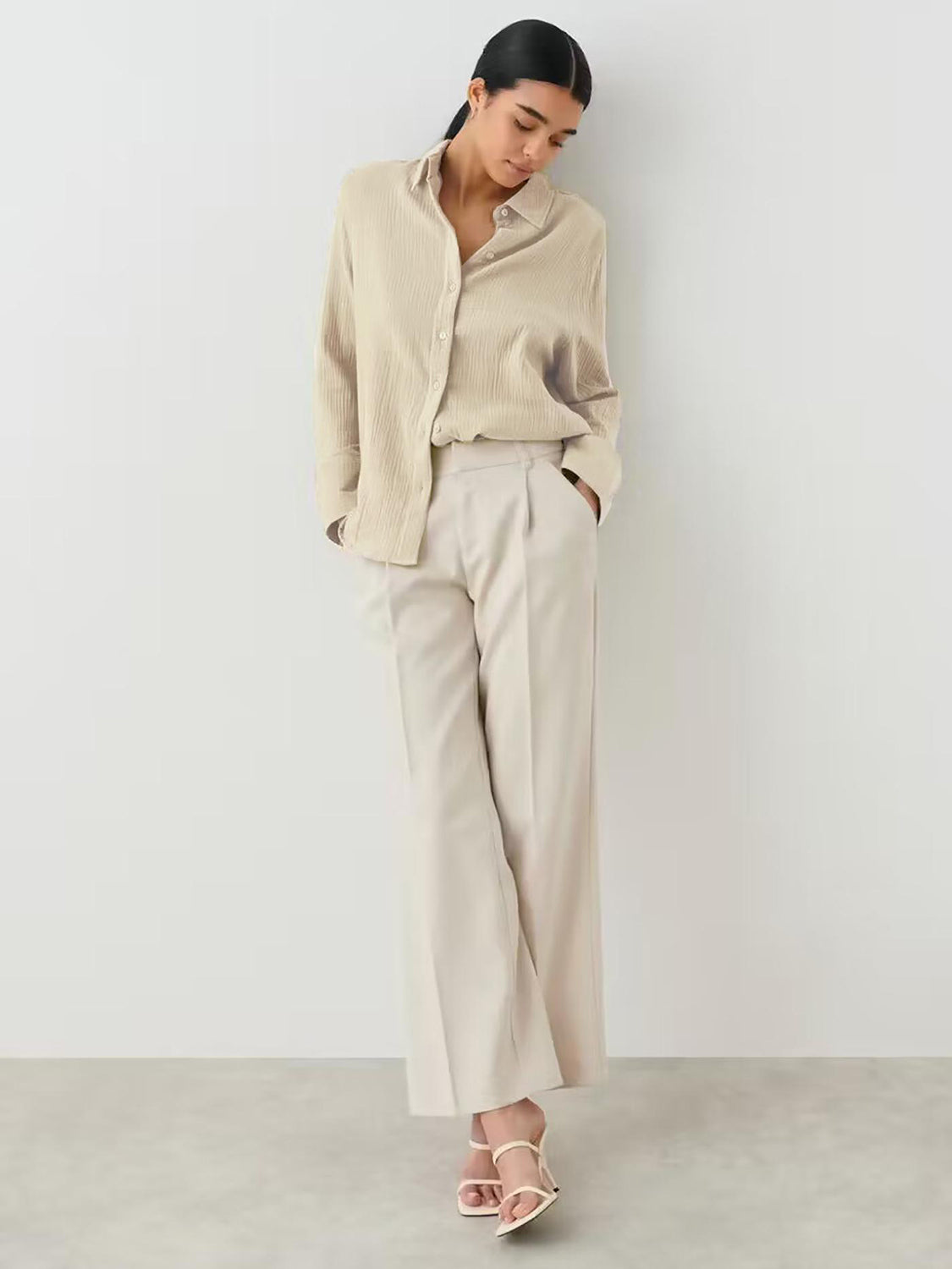 Beige textured cotton overshirt with relaxed fit and button front, styled with wide-leg trousers.
