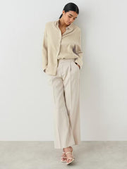 Beige textured cotton overshirt with relaxed fit and button front, styled with wide-leg trousers.