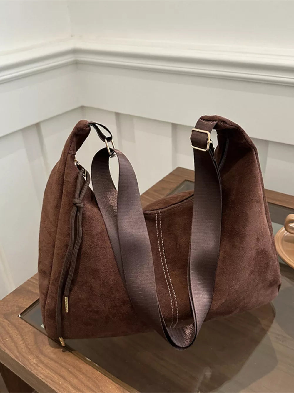 Brown suede crossbody bag with adjustable strap and drawstring detail