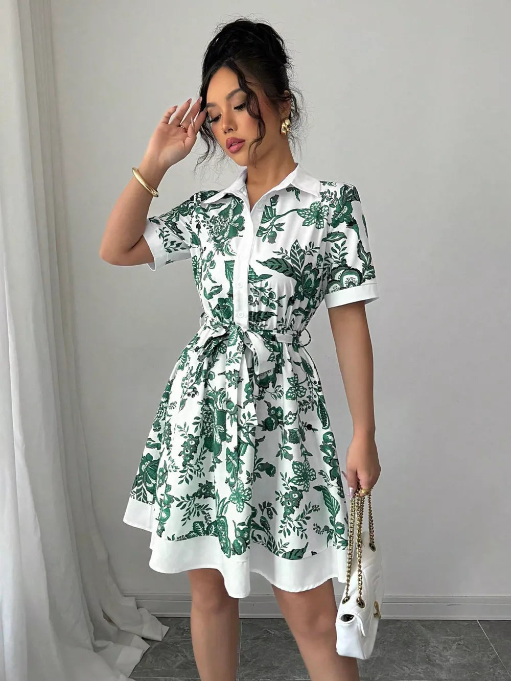 White mini dress with green floral print, collared, short sleeves, and tie belt.