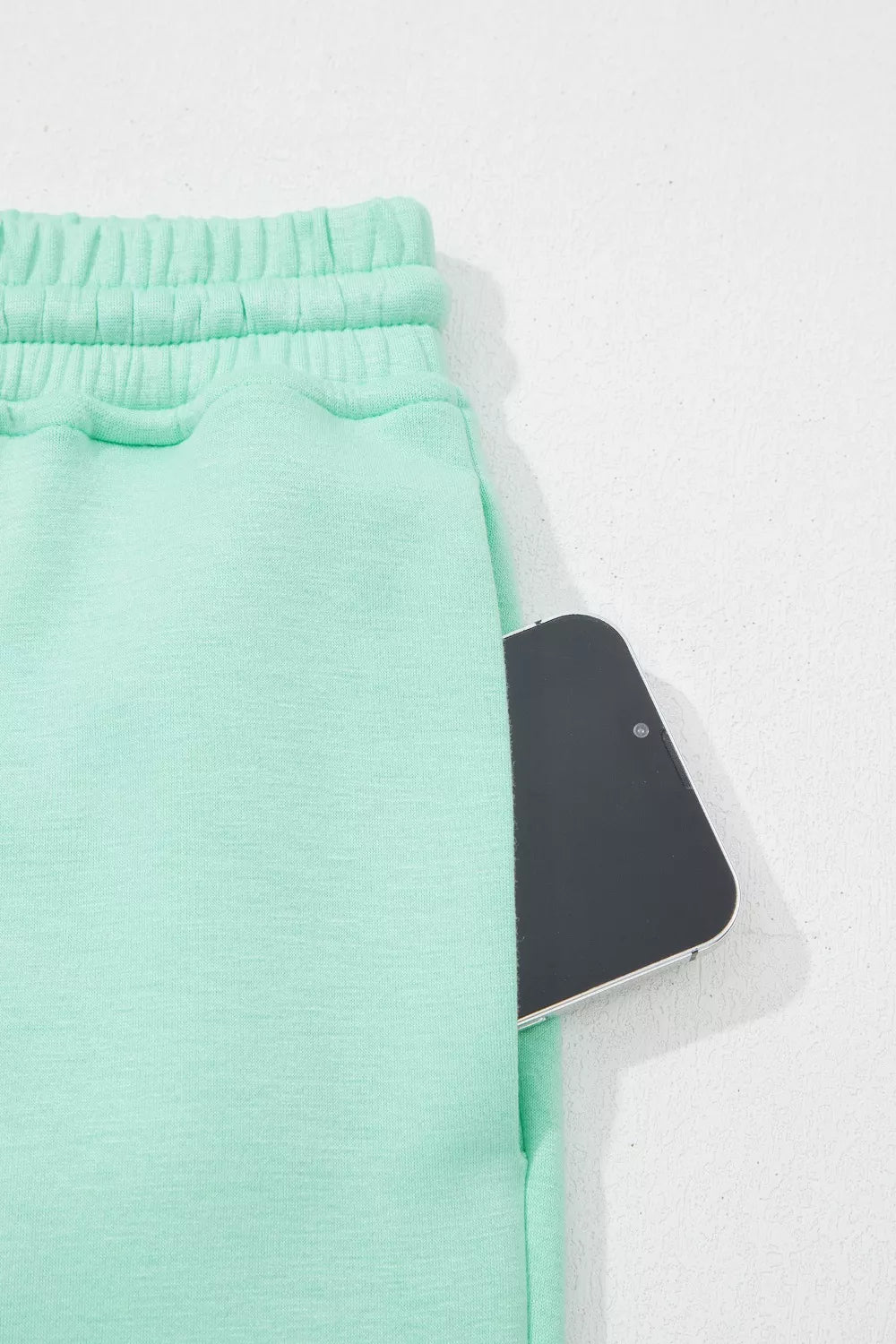 Mint green drawstring lounge pants with a pocket holding a smartphone.