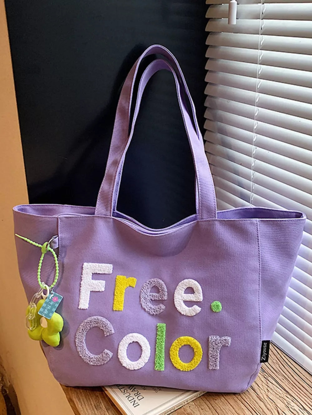 Lavender canvas shoulder bag with embroidered "Free Color" text and floral charm