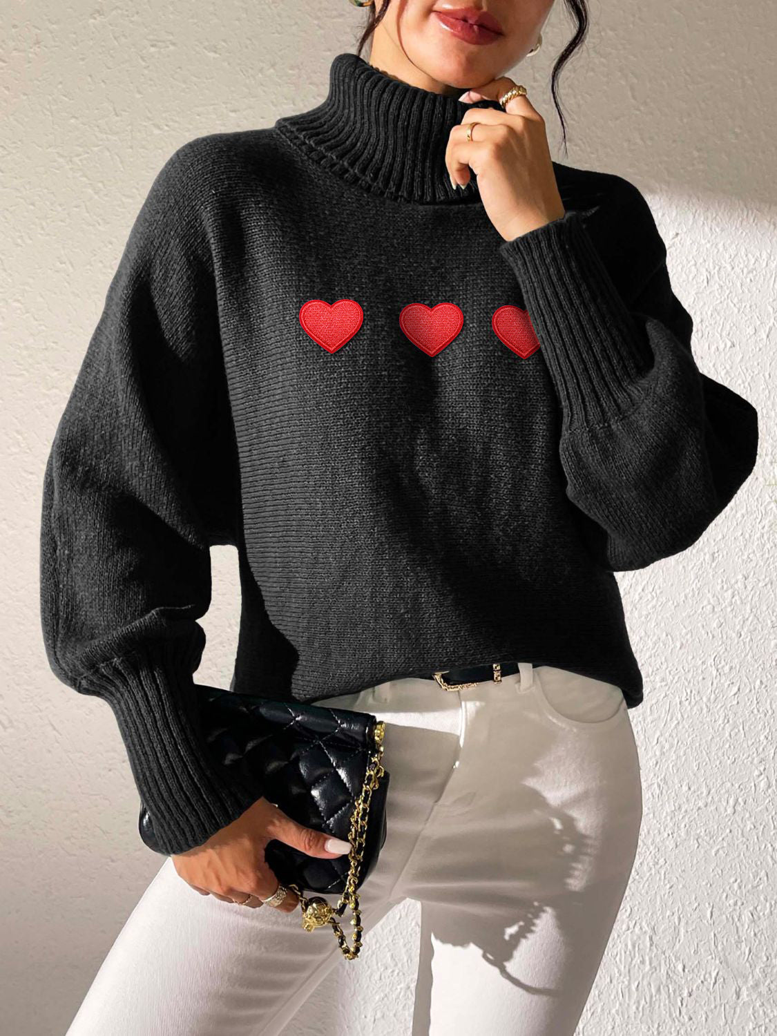 Black turtleneck sweater with balloon sleeves and red heart appliqués.