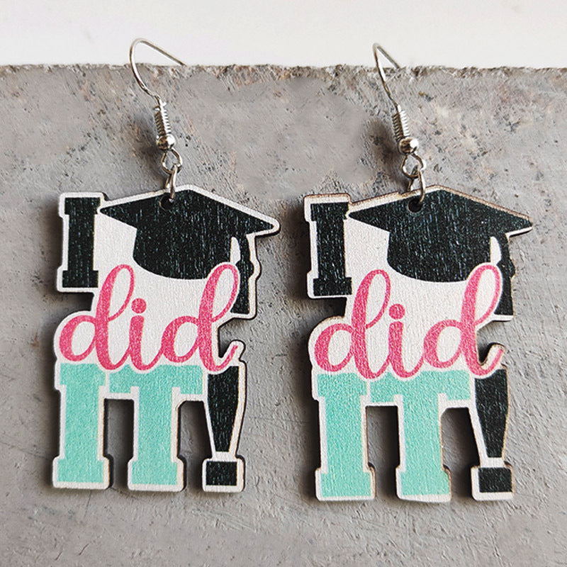 Graduation drop earrings with black caps, pink text, and teal accents.