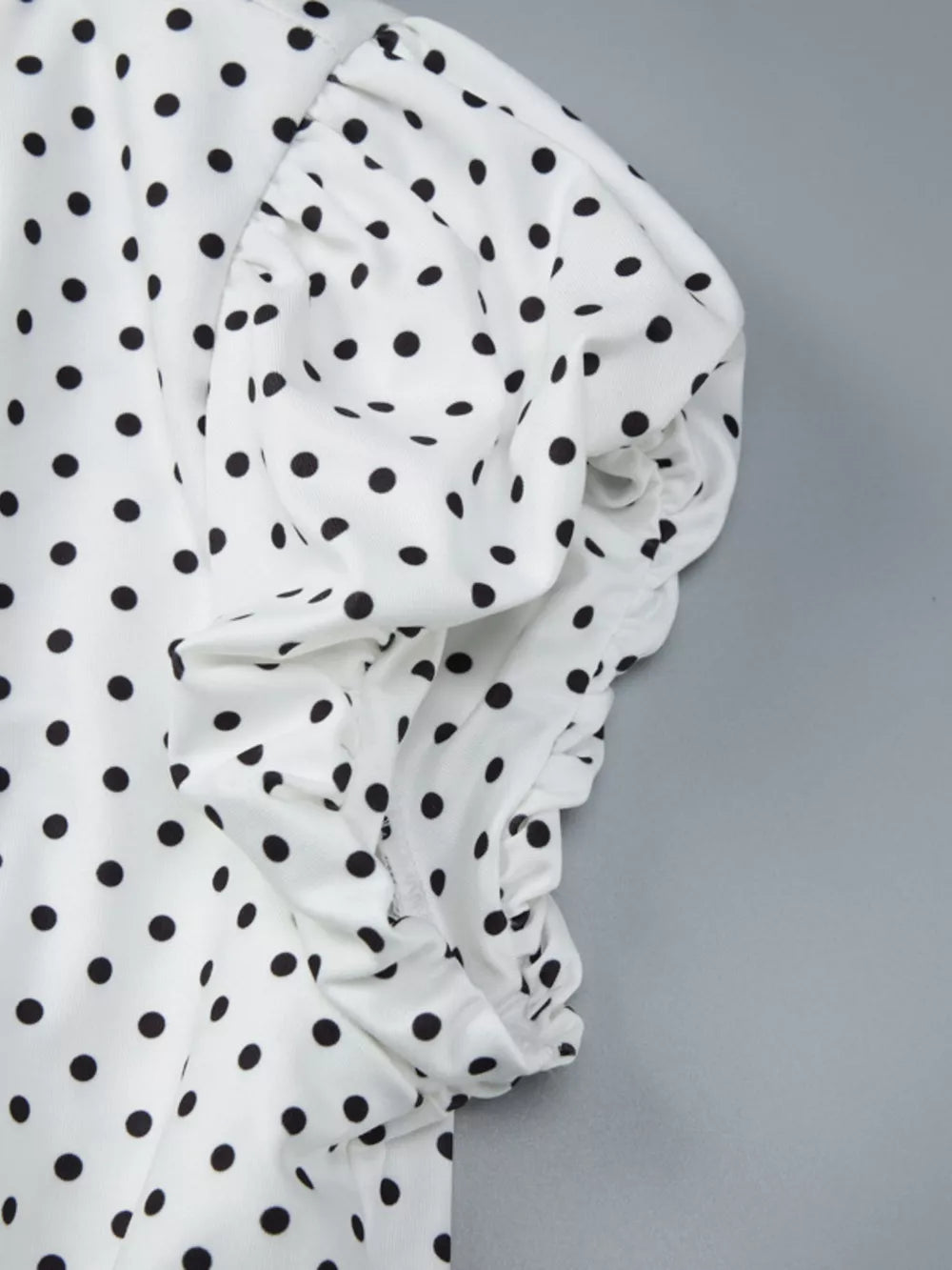 White t-shirt with black polka dots and ruched sleeve detail.
