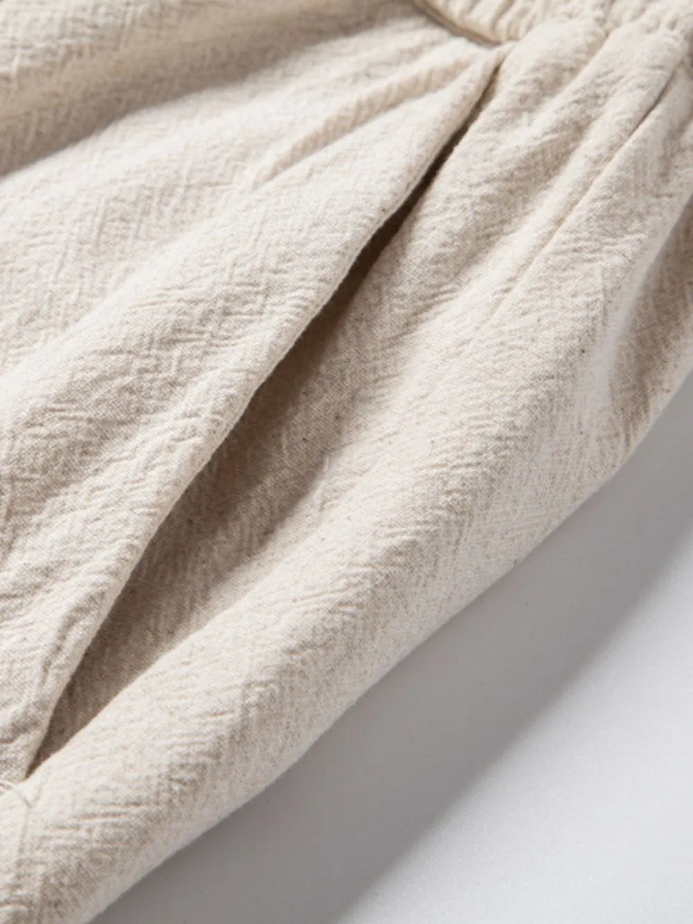 Pleated linen drawstring trousers in beige showing textured fabric and pocket detail.