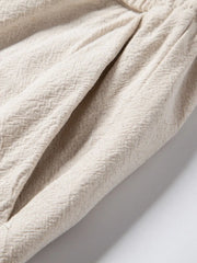 Pleated linen drawstring trousers in beige showing textured fabric and pocket detail.