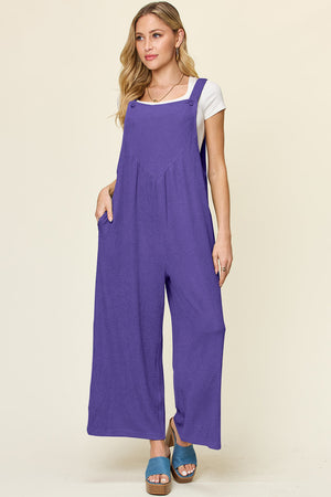 Ribbed wide-leg pinafore jumpsuit in purple with button straps and pockets.