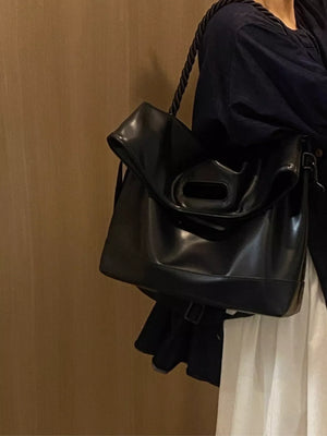 Black oversized PU leather tote bag with unique handle and rope strap detail.