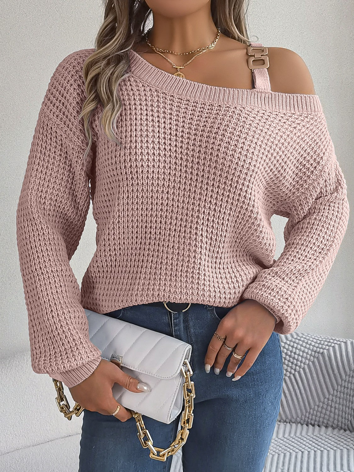 Blush pink one-shoulder knit sweater with buckle detail and waffle texture.