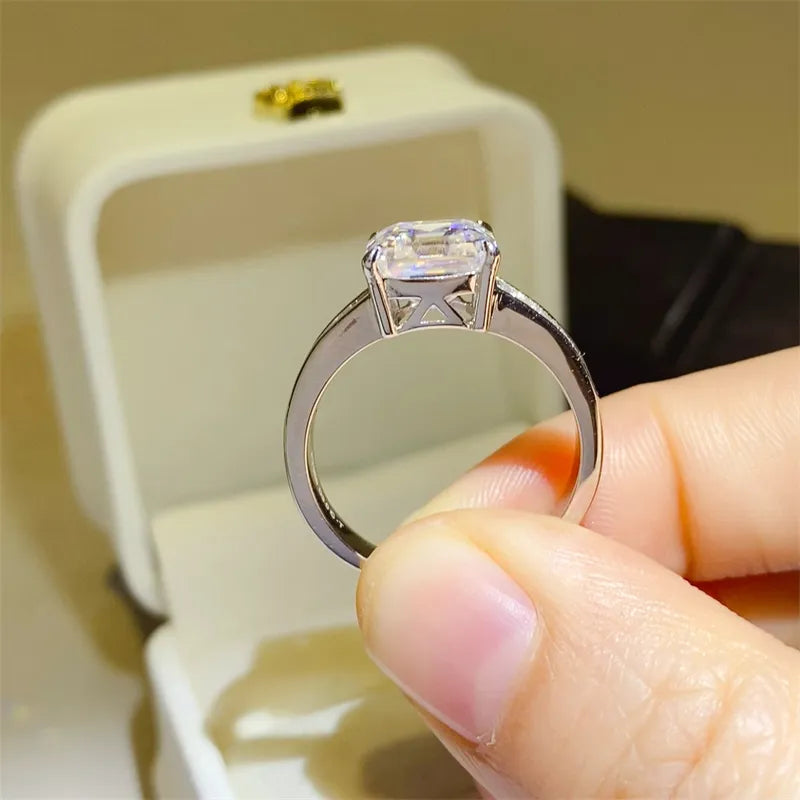 Silver ring with emerald cut diamond and baguette accents on a white ring box.