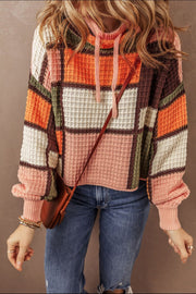 Waffle knit hoodie with colorblock patchwork in orange, pink, green, cream, and brown. Features a drawstring hood and ribbed