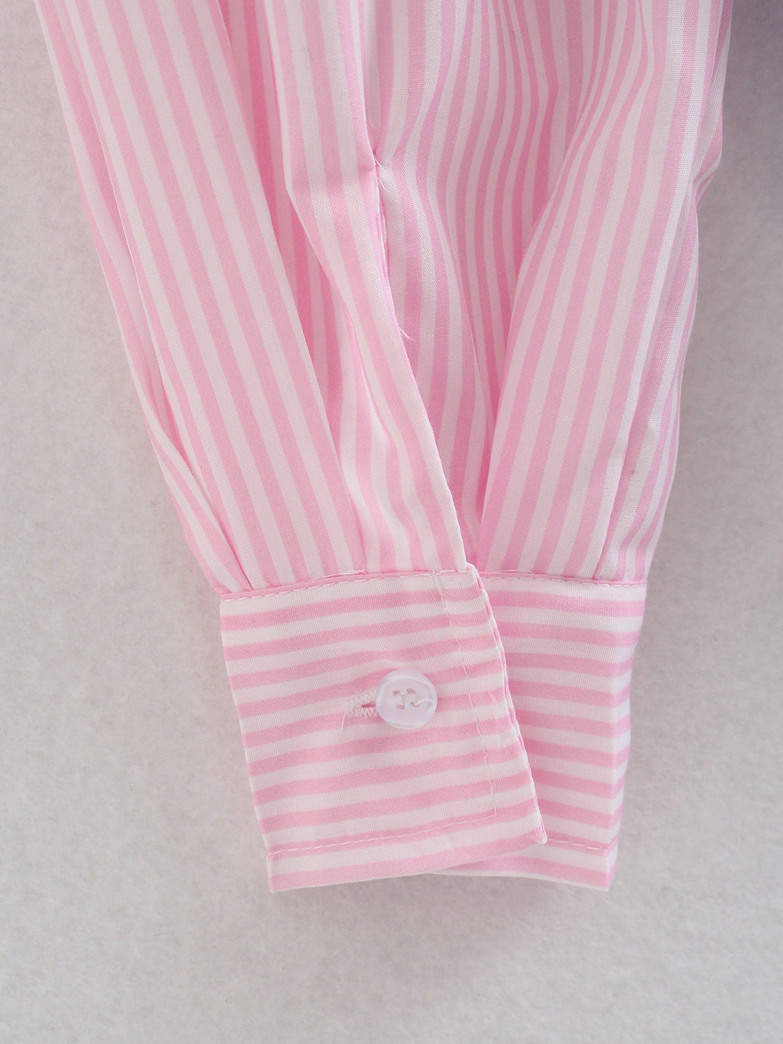 Blush pink and white striped oversized button-down shirt cuff detail with a white button.