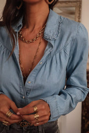 Indigo button-up blouse with ruffled collar and cinched sleeves.