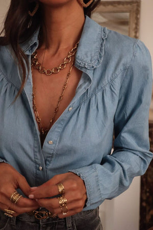 Indigo button-up blouse with ruffled collar and cinched sleeves.