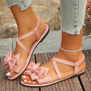 Pink crisscross bow sandals with ankle straps and elastic back.