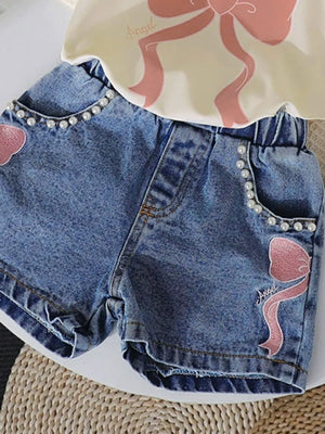 Baby denim shorts with pearl trim and pink bowknot embroidery, paired with a cream tee.