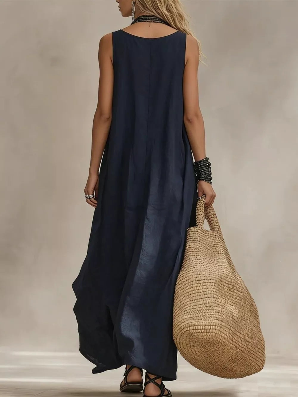 Dark blue sleeveless maxi dress with scoop neck, flowing skirt, and straw tote bag.