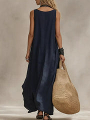 Dark blue sleeveless maxi dress with scoop neck, flowing skirt, and straw tote bag.