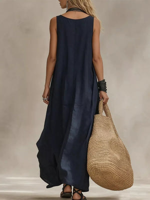 Dark blue sleeveless maxi dress with scoop neck, flowing skirt, and straw tote bag.
