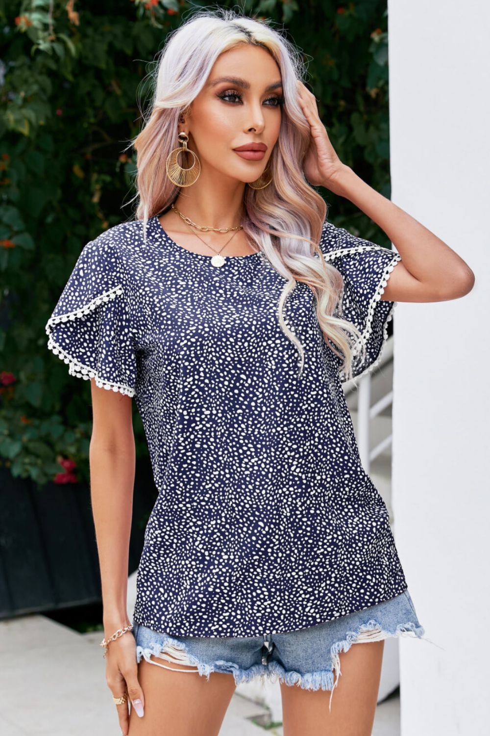 Dark blue dotted polyester blouse with flutter sleeves and pom-pom trim.