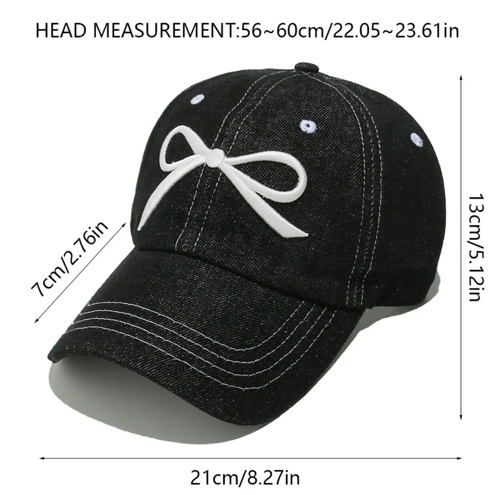 Black denim baseball cap with white embroidered bow detail and contrast stitching.