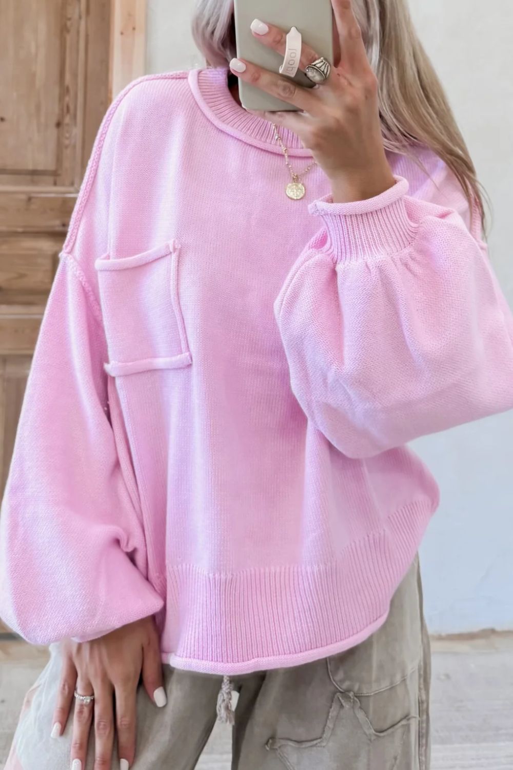 Pink knit sweater with puffed sleeves, contrast stitching, and a chest pocket.