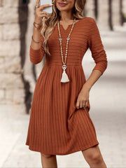 Ribbed knit A-line dress in rust with long sleeves and a V-neck, styled with a beaded necklace.