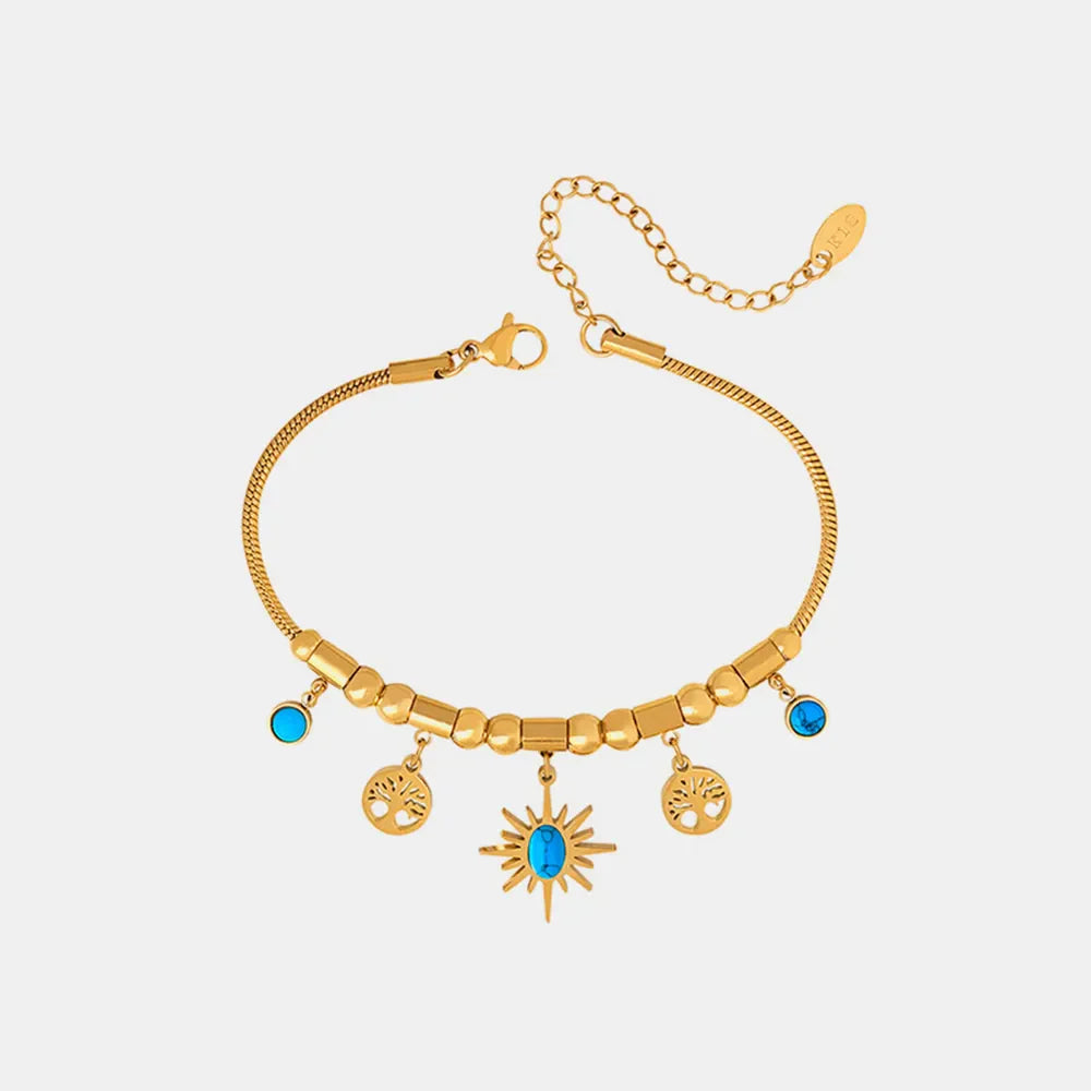 Gold celestial charm bracelet with turquoise accents, featuring sun and tree charms.