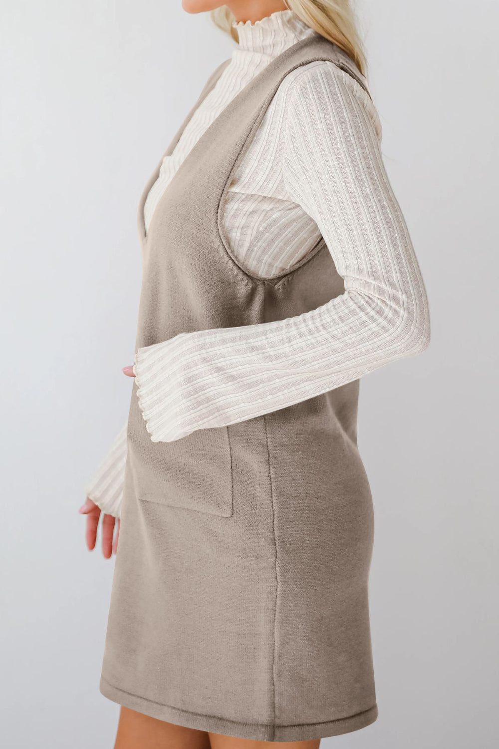 Sleeveless knit pocket dress in gray with V-neck, layered over a cream ribbed turtleneck.