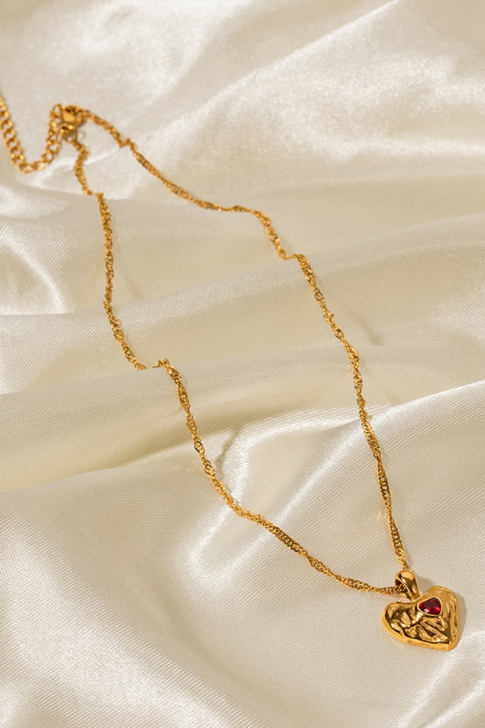 Gold textured heart pendant necklace with red stone on a delicate chain.