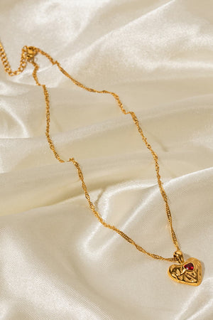 Gold textured heart pendant necklace with red stone on a delicate chain.