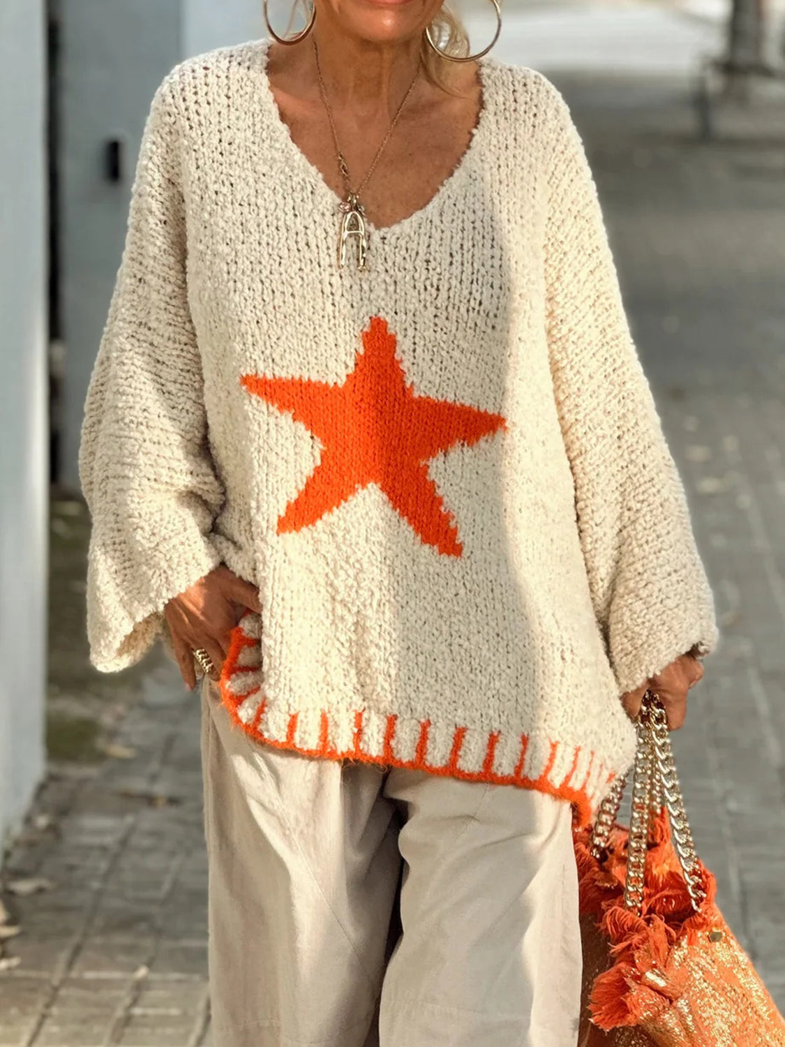 Cream knit v-neck pullover with orange star detail and ribbed hem.