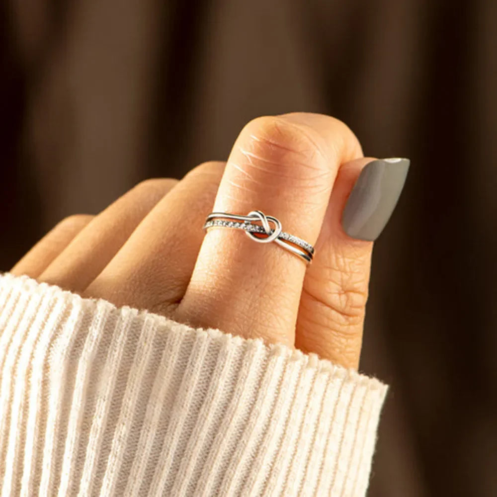 Silver knot ring with pavé detail on a finger, styled with a cream sweater.