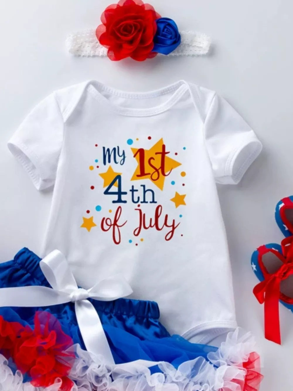 White baby onesie with "my 1st 4th of July" graphic, blue tutu, and patriotic headband.