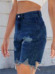 Distressed denim bermuda shorts in dark wash with frayed hem and rips.