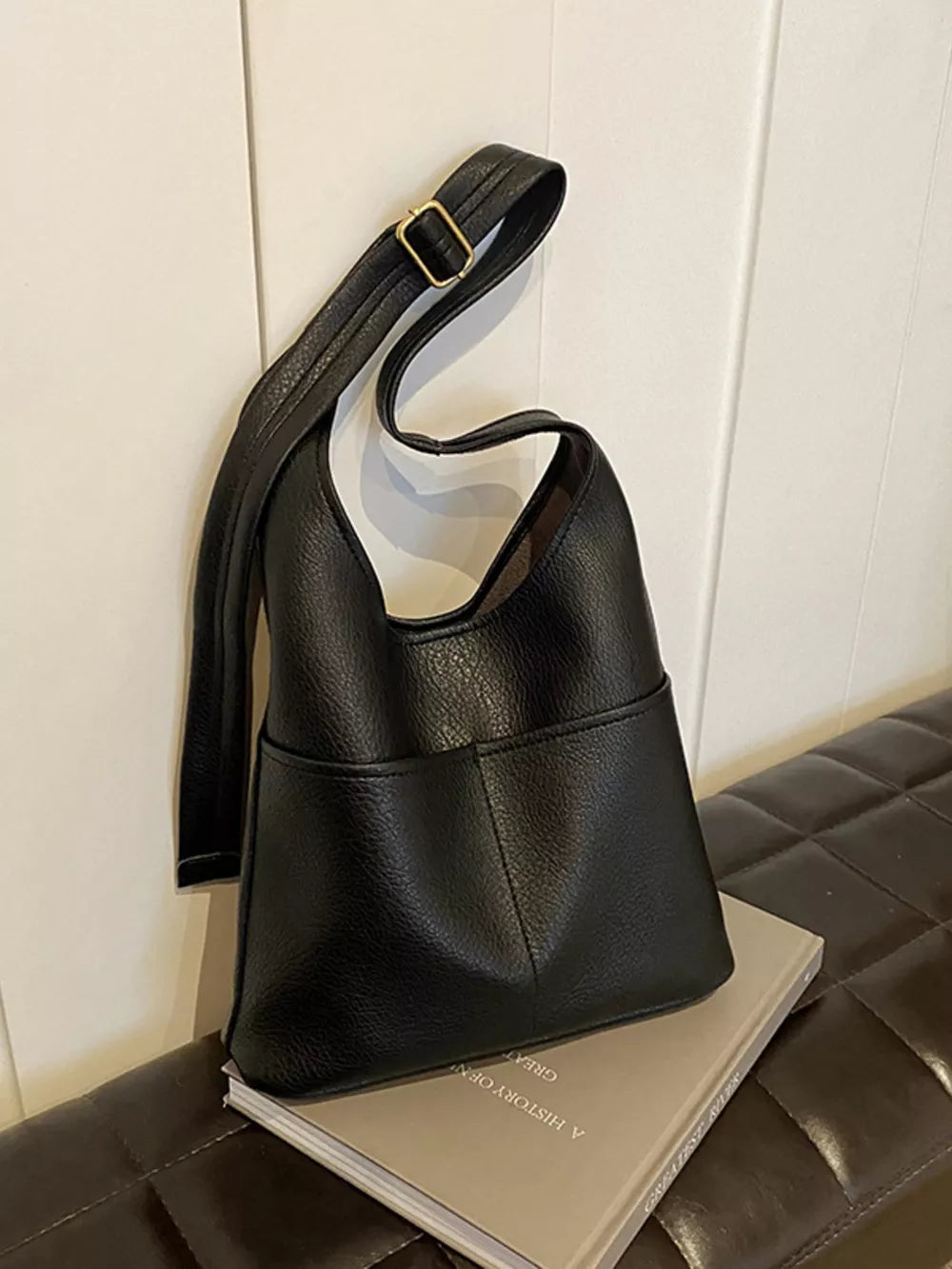 Black textured PU leather shoulder bag with adjustable strap and front pocket detail.