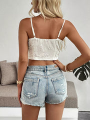 White lace camisole with floral embroidery and ruffle hem, paired with distressed denim shorts.