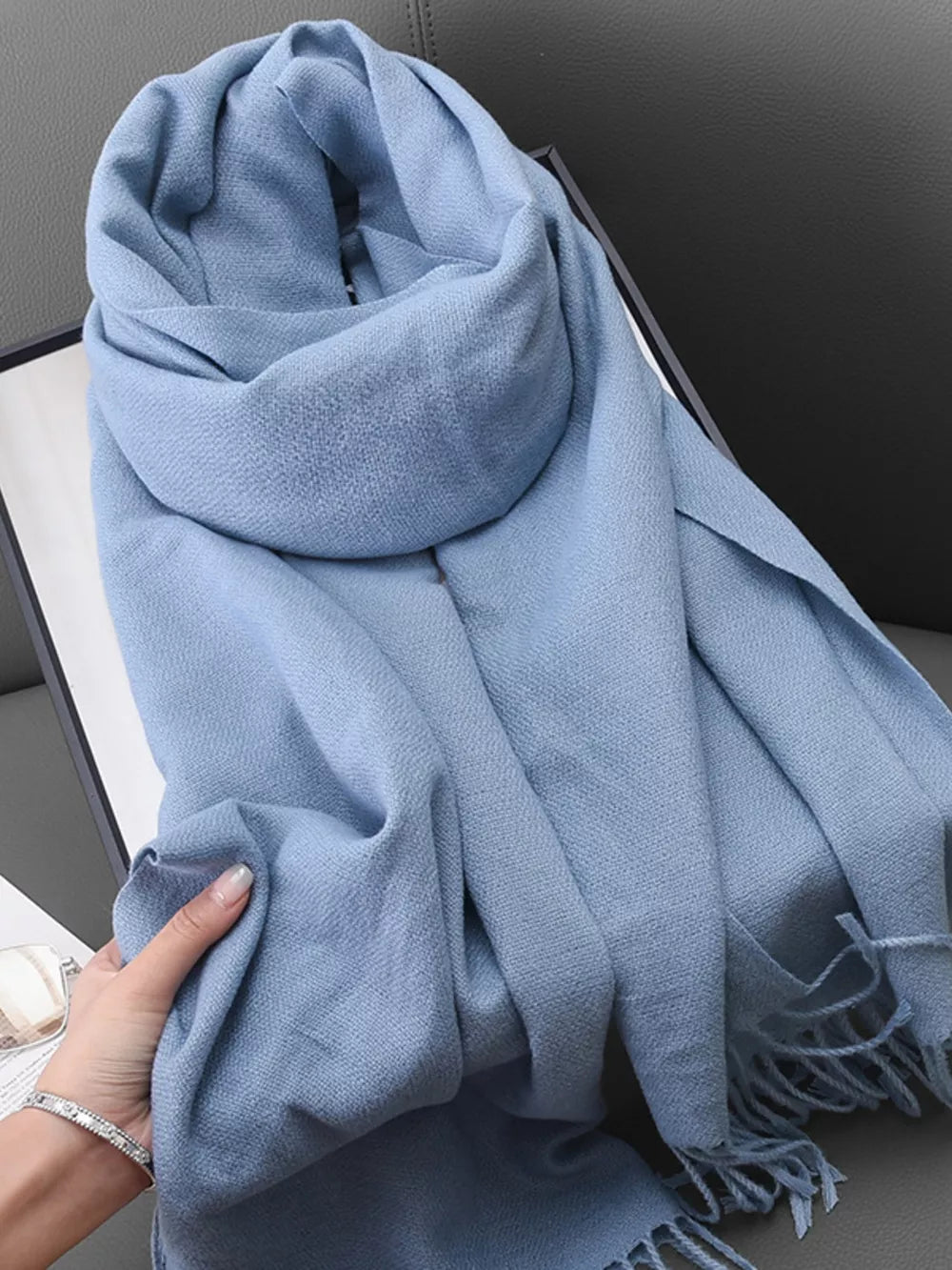Light blue textured scarf with fringe detail, styled loosely.